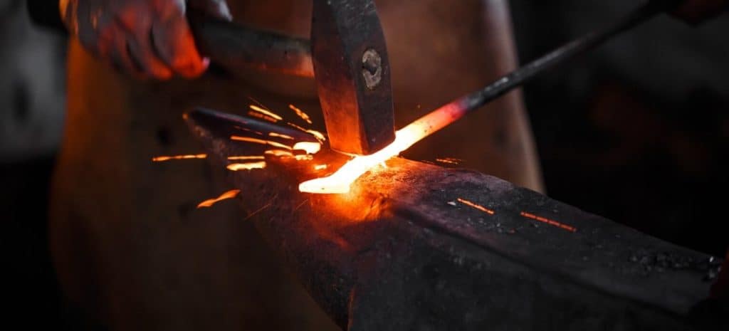A blacksmith hammer molding a red-hot item with sparks flying.